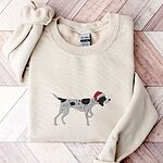 Sand crewneck sweatshirt laid flat on a herringbone wood floor, embroidered with a black and white ticked German shorthaired pointer in a red Santa hat