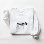 White crewneck sweatshirt laid flat on a white background, embroidered with a black and white ticked German shorthaired pointer in a red Santa hat