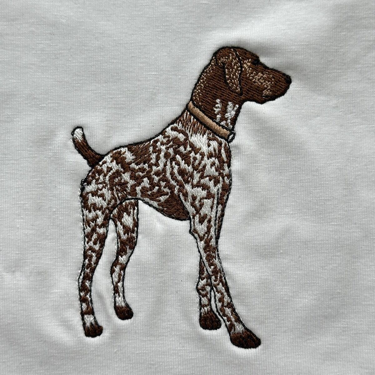 German Shorthaired Pointer Embroidery Close-Up Close-up of a real stitched German shorthaired pointer with a liver brown head, a white ticked coat, a tan collar and a fine black outline, on white fabric