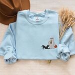 Light Blue crewneck sweatshirt laid flat with a brown hat and dried wheat, embroidered with a ghost sipping iced coffee with a black pit bull in a play bow on the left chest