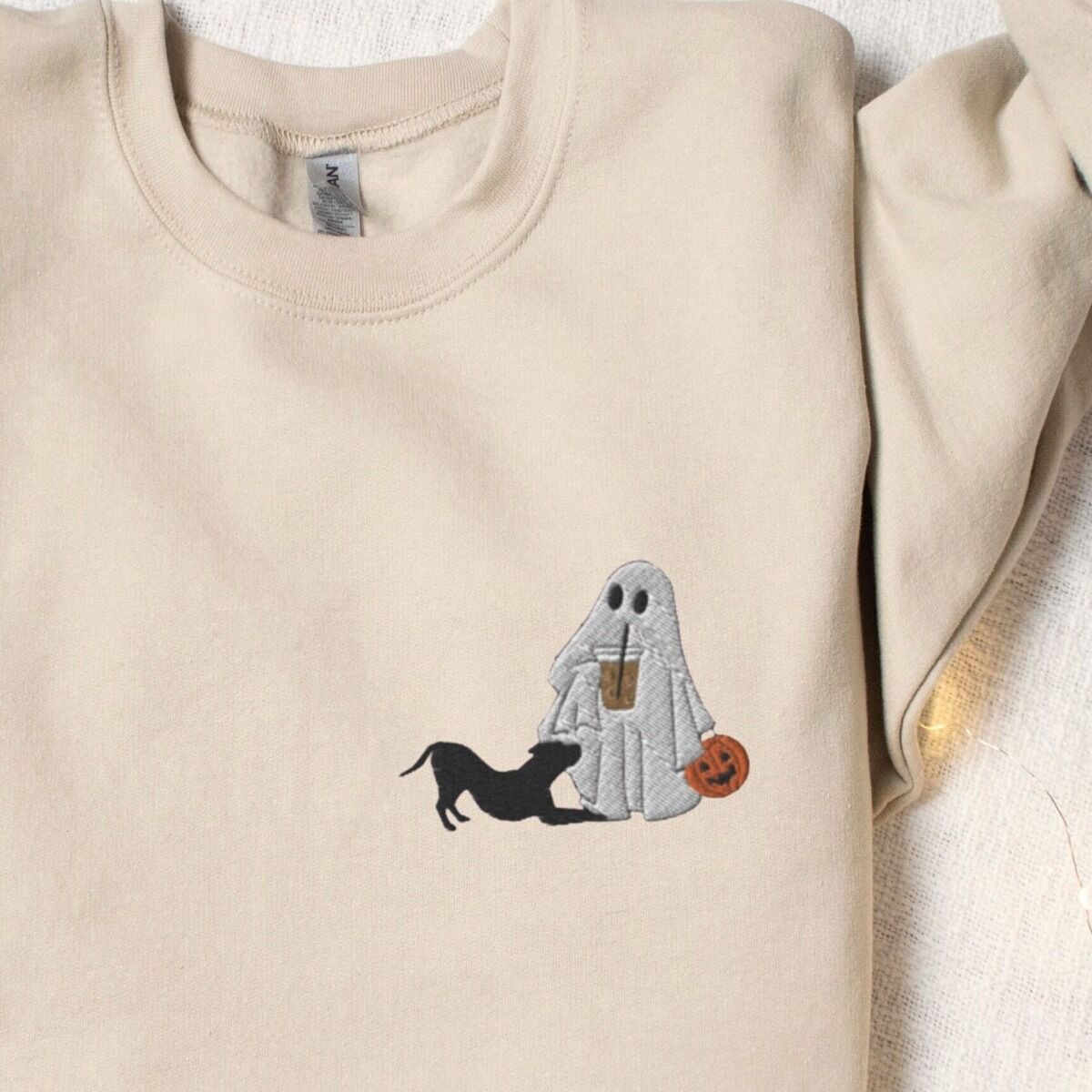 Ghost and Pitbull Sweatshirt – Sand Sand crewneck sweatshirt laid flat with a rolled cuff, embroidered with a ghost sipping iced coffee with a black pit bull in a play bow on the left chest