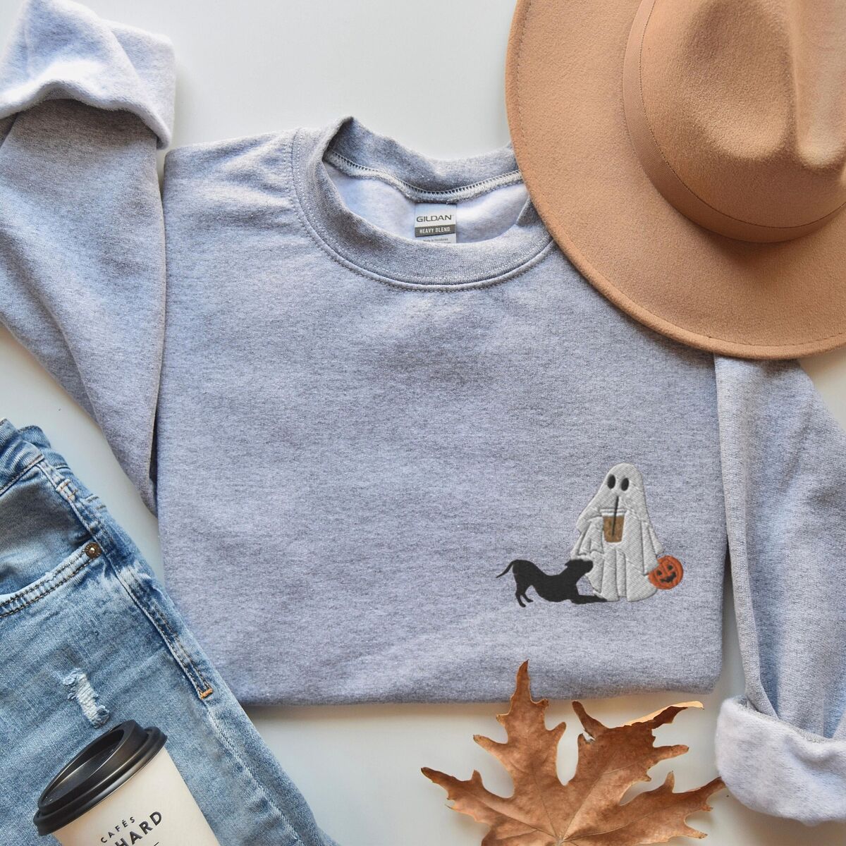 Ghost and Pitbull Sweatshirt - Sport Grey Sport Grey crewneck sweatshirt laid flat with jeans, a coffee cup, a felt hat and fall leaves, embroidered with a ghost sipping iced coffee with a black pit bull in a play bow on the left chest