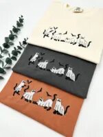 Three embroidered ghost cat T-shirts in Ivory, Pepper and Yam laid in a row