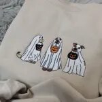 Close-up of the embroidered ghost dogs, a golden pup, a brown dog with an orange pumpkin pail and a white dog with brown ears
