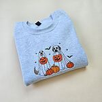 Ash crewneck sweatshirt folded on a pale yellow background, embroidered with two dogs in white ghost sheets holding jack-o'-lantern buckets among pumpkins, with bats and stars