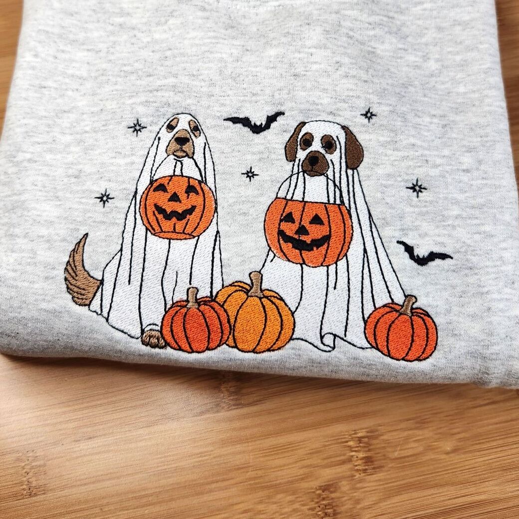 Ghost Dogs with Pumpkins Sweatshirt – Ash on Wood Folded Ash ghost dogs with pumpkins sweatshirt on a wooden table, two dogs in ghost sheets with jack-o'-lantern buckets among pumpkins