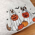 Close-up of the embroidery on an Ash ghost dogs with pumpkins sweatshirt: a golden dog and a brown and white dog in ghost sheets holding jack-o'-lantern buckets, pumpkins, bats and stars