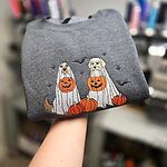 Dark Heather ghost dogs with pumpkins sweatshirt held up by hand, stitched with custom coat colors: a golden dog and a yellow dog in ghost sheets