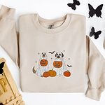 Sand crewneck sweatshirt laid flat with a skull, an RIP tombstone and black paper butterflies, embroidered with two dogs in white ghost sheets holding jack-o'-lantern buckets among pumpkins, with bats and stars