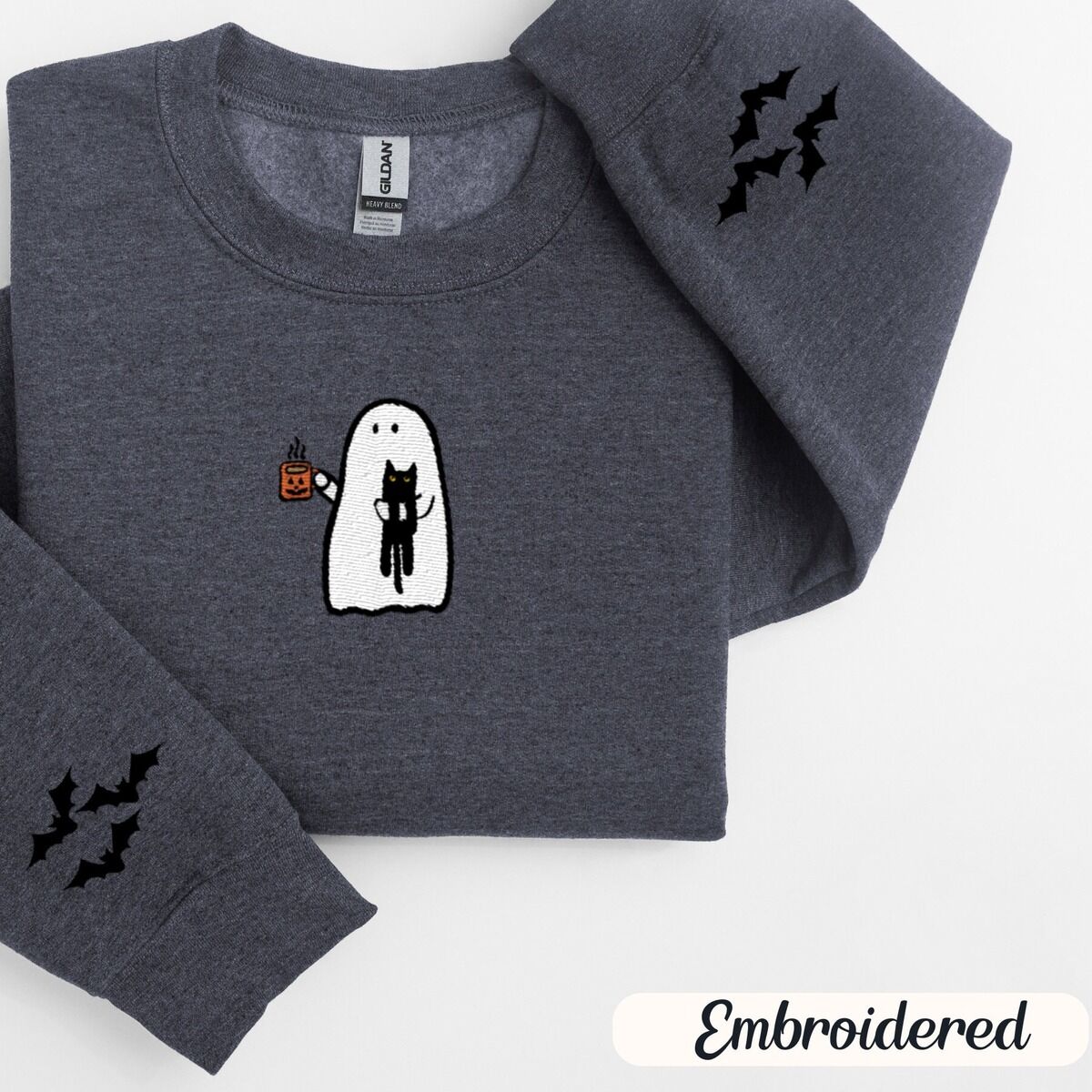Ghost Drinking Coffee Sweatshirt – Dark Heather Dark Heather crewneck sweatshirt folded on a white background, embroidered with a white ghost hugging a black cat and holding a steaming jack-o'-lantern coffee mug, with small bats on the sleeves