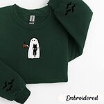 Forest Green crewneck sweatshirt folded on a white background, embroidered with a white ghost hugging a black cat and holding a steaming jack-o'-lantern coffee mug, with small bats on the sleeves