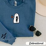 Indigo Blue crewneck sweatshirt folded with a cream hat and sunglasses, embroidered with a white ghost hugging a black cat and holding a steaming jack-o'-lantern coffee mug, with small bats on the sleeves