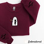 Maroon crewneck sweatshirt folded on a white background, embroidered with a white ghost hugging a black cat and holding a steaming jack-o'-lantern coffee mug, with small bats on the sleeves