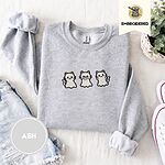 Ash crewneck sweatshirt folded with denim shorts, white sneakers and a potted plant, embroidered with three white ghost kittens with pink cheeks and black outlines