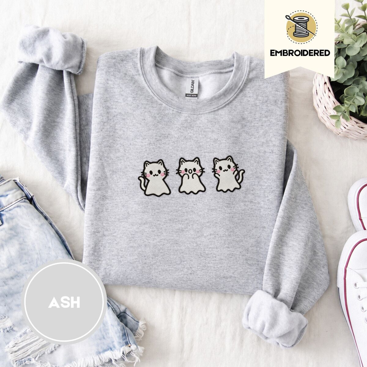Ghost Kitten Sweatshirt – Ash Ash crewneck sweatshirt folded with denim shorts, white sneakers and a potted plant, embroidered with three white ghost kittens with pink cheeks and black outlines
