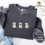 Dark Heather crewneck sweatshirt folded with ripped jeans and a silver chain necklace, embroidered with three white ghost kittens with pink cheeks and black outlines