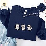 Navy crewneck sweatshirt folded with ripped jeans and a silver chain necklace, embroidered with three white ghost kittens with pink cheeks and black outlines