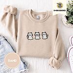 Sand crewneck sweatshirt folded with denim shorts, white sneakers and a potted plant, embroidered with three white ghost kittens with pink cheeks and black outlines