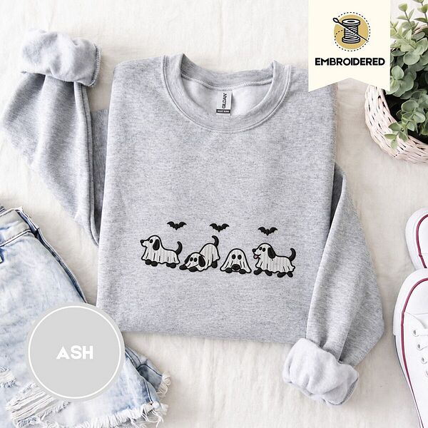 Ash crewneck sweatshirt folded with denim shorts, white sneakers and a potted plant, embroidered with four puppies in white ghost sheets with black floppy ears and tails under three flying black bats