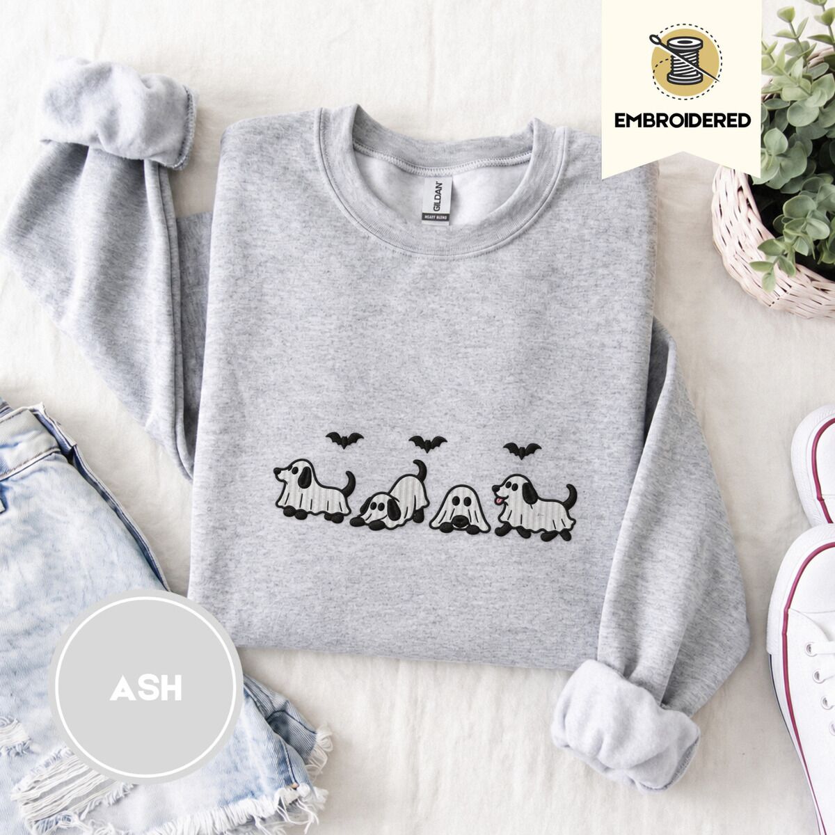 Ghost Puppy Sweatshirt – Ash Ash crewneck sweatshirt folded with denim shorts, white sneakers and a potted plant, embroidered with four puppies in white ghost sheets with black floppy ears and tails under three flying black bats