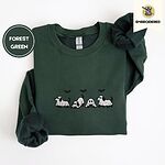 Forest Green crewneck sweatshirt folded on a white background, embroidered with four puppies in white ghost sheets with black floppy ears and tails under three flying black bats
