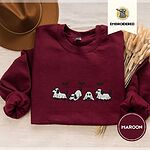 Maroon crewneck sweatshirt with a brown felt hat and dried bunny tail grass, embroidered with four puppies in white ghost sheets with black floppy ears and tails under three flying black bats