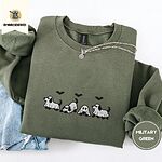 Military Green crewneck sweatshirt folded with light jeans and a silver chain necklace, embroidered with four puppies in white ghost sheets with black floppy ears and tails under three flying black bats
