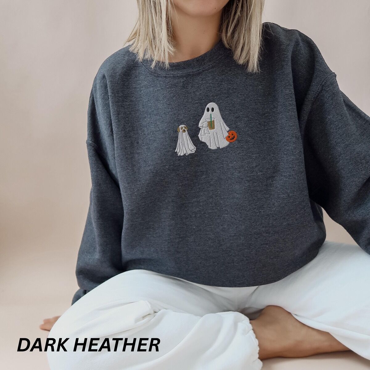 Ghost Walking Dog Sweatshirt – Dark Heather Woman sitting in a Dark Heather crewneck sweatshirt embroidered with a ghost sipping iced coffee and carrying a jack-o'-lantern pail while walking a little yellow lab in a ghost sheet on a leash