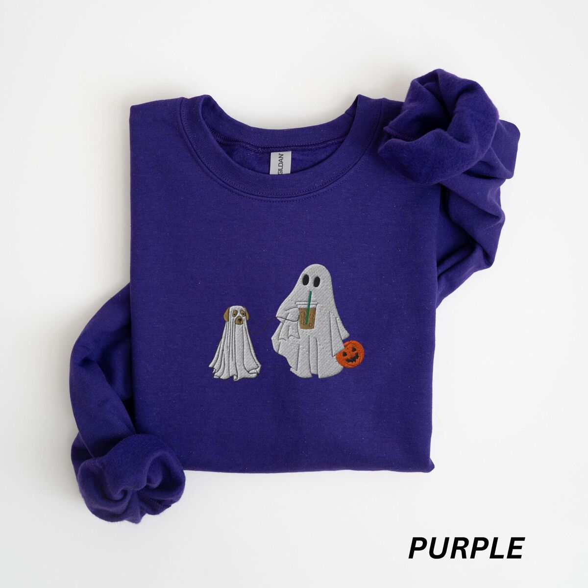 Ghost Walking Dog Sweatshirt - Purple Purple crewneck sweatshirt laid flat on a white background, embroidered with a ghost sipping iced coffee and carrying a jack-o'-lantern pail while walking a little yellow lab in a ghost sheet on a leash