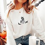 Woman with a pumpkin necklace in a White crewneck sweatshirt embroidered with a ghost covered in black cats, one draped over its head, one in its arms, one climbing its side and two stretching at its feet
