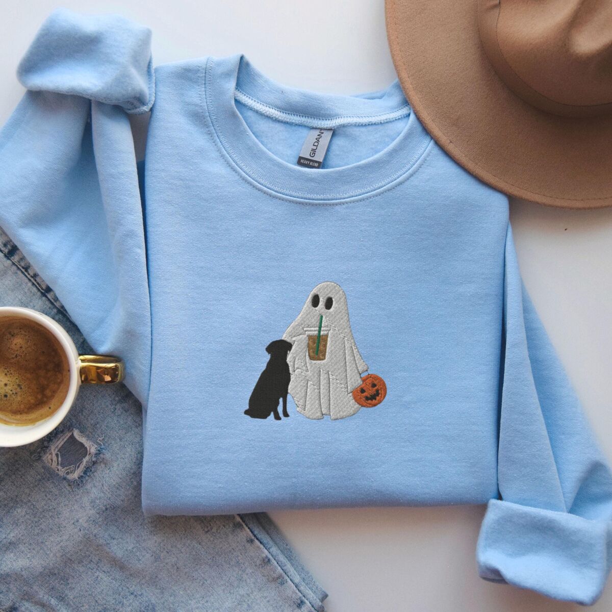 Ghost with Black Lab Sweatshirt - Light Blue Light Blue crewneck sweatshirt laid flat beside jeans and a coffee cup, embroidered with a ghost lab mom sipping iced coffee and carrying a jack-o'-lantern pail, with a black lab sitting against her