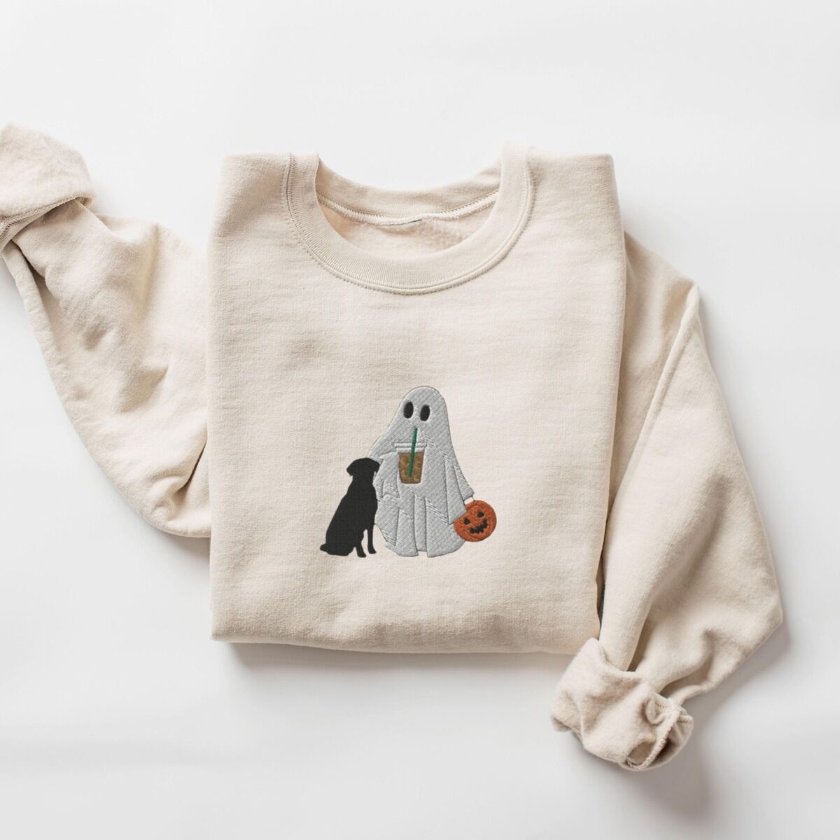 Ghost with Black Lab Sweatshirt – Sand Sand crewneck sweatshirt laid flat on a white background, embroidered with a ghost lab mom sipping iced coffee and carrying a jack-o'-lantern pail, with a black lab sitting against her