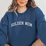 Woman in an Indigo Blue crewneck sweatshirt embroidered with GOLDEN MOM in arched white varsity letters