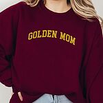 Woman in a Maroon crewneck sweatshirt embroidered with GOLDEN MOM in arched mustard gold varsity letters