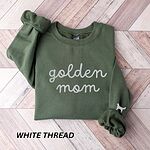 Military Green crewneck sweatshirt laid flat on wood, embroidered with golden mom in white script and a golden retriever silhouette on the cuff