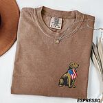Espresso T-shirt folded with a necklace, a golden retriever with a stars-and-stripes flag stitched on the left chest