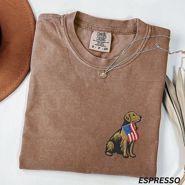 Espresso T-shirt folded with a necklace, a golden retriever with a stars-and-stripes flag stitched on the left chest