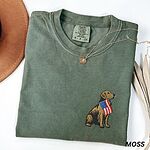 Moss T-shirt folded beside a hat, a sitting golden retriever with a USA flag stitched on the left chest