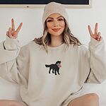 Woman in a beanie making peace signs in a sand crewneck sweatshirt with a golden retriever carrying a flag