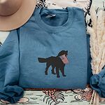 Indigo Blue crewneck sweatshirt beside a hat and dried grass, embroidered with a golden retriever carrying an American flag