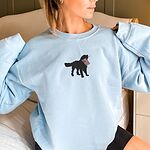 Woman in a Light Blue crewneck sweatshirt with a black golden retriever holding a USA flag centered on the chest