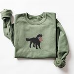 Military Green crewneck sweatshirt laid flat, a black golden retriever holding a stars-and-stripes flag stitched across the chest