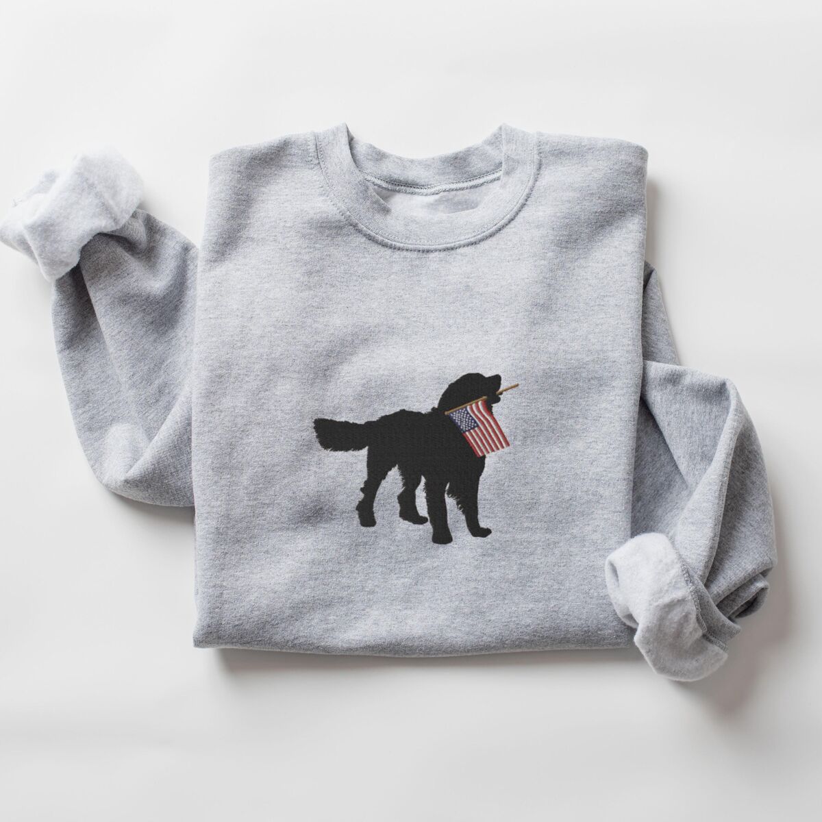 Golden Retriever American Flag Sweatshirt - Sport Grey Sport Grey crewneck sweatshirt laid flat with rolled sleeves, a golden retriever silhouette with an American flag stitched in the center