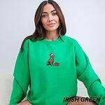 Woman sitting in an Irish Green crewneck sweatshirt embroidered with a golden retriever in a Santa hat next to a red present