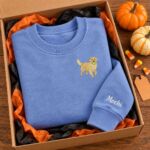Blue golden retriever crewneck with the name Mochi on the sleeve in a gift box with orange tissue paper and pumpkins