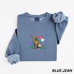 Blue Jean crewneck sweatshirt laid flat, embroidered with a sitting golden retriever among spring flowers and a pink butterfly