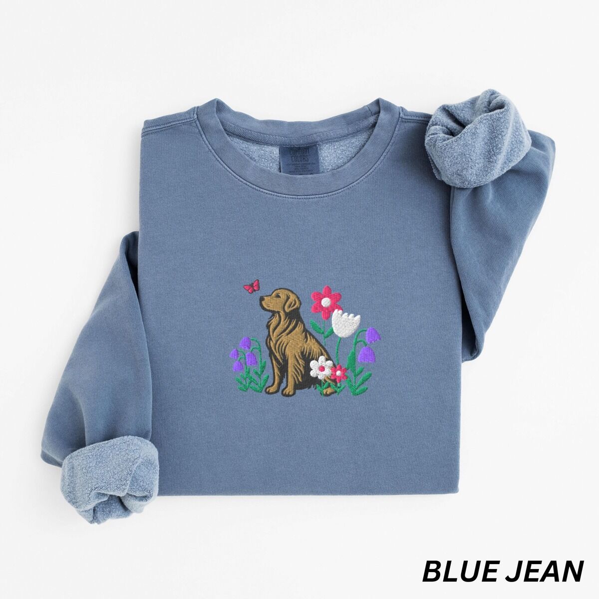 Golden Retriever Flower Sweatshirt – Blue Jean Blue Jean crewneck sweatshirt laid flat, embroidered with a sitting golden retriever among spring flowers and a pink butterfly