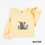Butter crewneck sweatshirt laid flat with a rolled cuff, embroidered with a sitting golden retriever among pink daisies, a white tulip and purple bellflowers