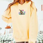 Woman in an oversized Butter crewneck sweatshirt embroidered with a sitting golden retriever among spring flowers