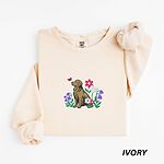 Ivory crewneck sweatshirt laid flat, embroidered with a sitting golden retriever among spring flowers and a pink butterfly